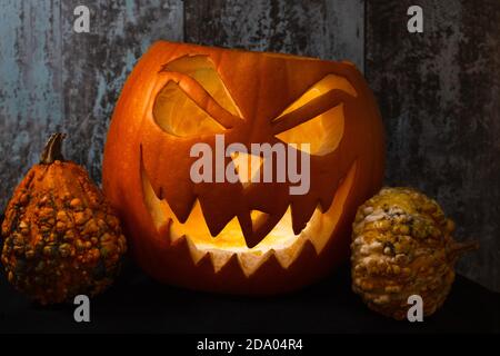 Jack O'Lantern carved pumpkin with evil face and miniature pumpkins on a wooden background- Halloween tradition Stock Photo