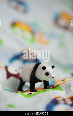 Closeup of a small panda toy placed on a colorful fabric with owls on a white background Stock Photo