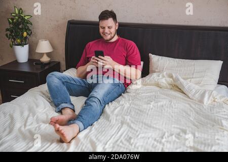 man sitting in bed surfing internet on the phone Stock Photo