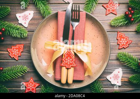 Top view of cutlery and plate on festive wooden background. New Year family dinner concept. Fir tree and Christmas decorations. Stock Photo