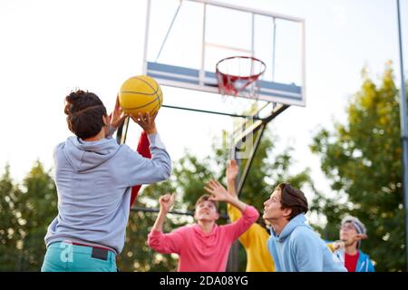 group of young male teenagers in colourful hoodies playing basketball outdoors in the street Stock Photo