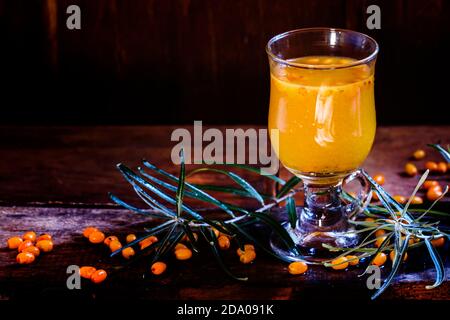 Sea buckthorn hot drink in a glass, fresh berries scattered on brown old wooden background. Low key, selective focus. Stock Photo