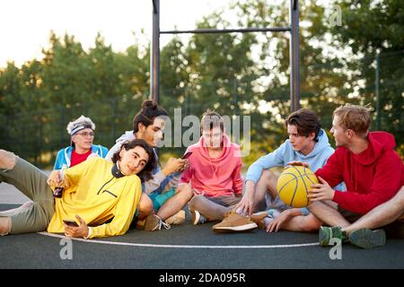 caucasian teens, basketball players sitting and resting in timeout, enjoying outdoor games, happy youth lifestyle. in city Stock Photo