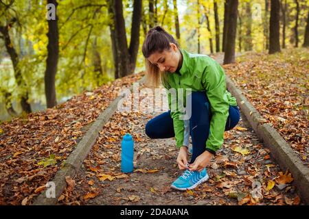 Runner tying shoe laces in autumn park. Woman training with water bottle. Active healthy sportive lifestyle Stock Photo