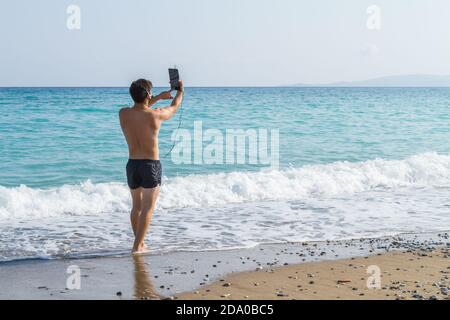 Young man using headphones and tablet. Attractive young maln wearing headphones and using a tablet at the beach. Lifestyle, and digital communication Stock Photo