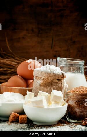 Baking ingredients: milk, butter, flour, sugar, eggs and rolling pin on a floured table in a rustic style, selective focus Stock Photo