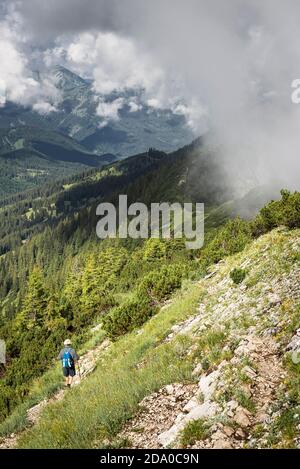 Elderly hiker on the trail along the sharp ridge of the Blue Mountains with clouds rising up in the air, Bavaria, Germany Stock Photo