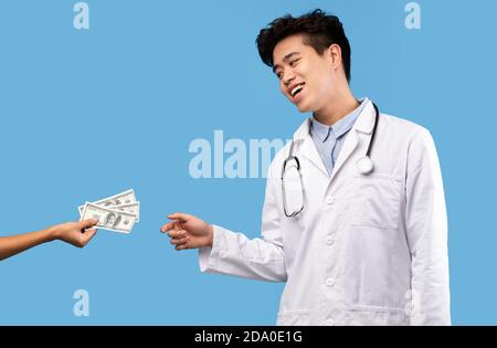 Greedy asian male doctor taking bribe from female patient Stock Photo