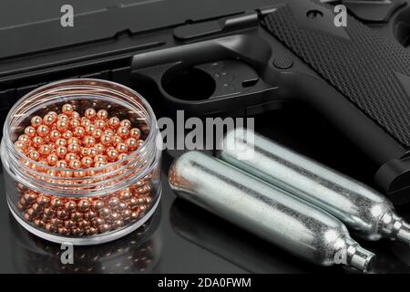 gas airsoft pistol, co2 cartridges and metal pellets close up on black Stock Photo