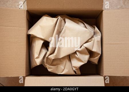 Crumpled wrapping craft brown paper in open after delivery paperboard box. Horizontal. Delivery, ecology, plastic free, resource overrun concept. Flat Stock Photo