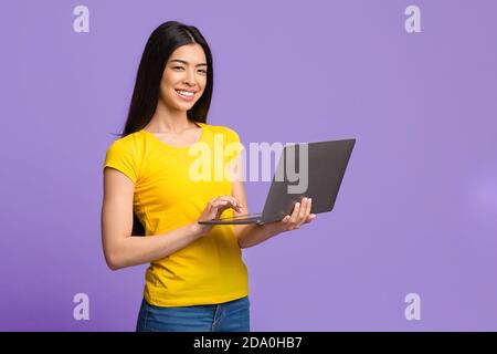 Positive Young Asian Woman Posing With Laptop Computer Over Purple Background Stock Photo