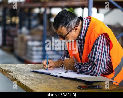 Side view adult worker wearing uniform writing on clipboard while working in spacious storehouse Stock Photo