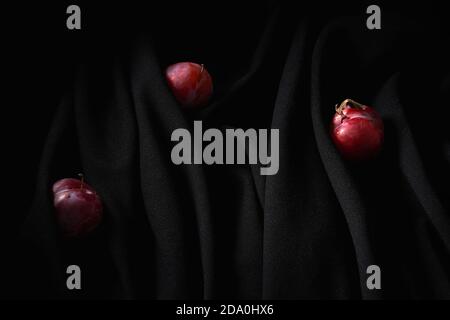 Red small cherries on thin stems placed on dark black wrinkled cloth in studio Stock Photo