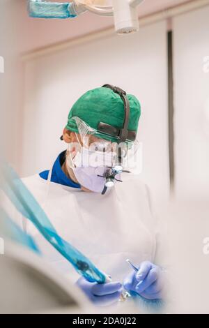 Unrecognizable male orthodontist in mask and protective glasses working near medical equipment in clinic Stock Photo