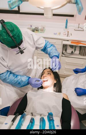 Unrecognizable orthodontist in sterile gloves putting transparent braces on teeth of Woman in clinic Stock Photo
