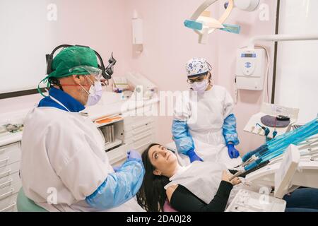 From above of anonymous stomatologist and assistant in uniforms talking to Woman lying on medical chair near professional equipment Stock Photo