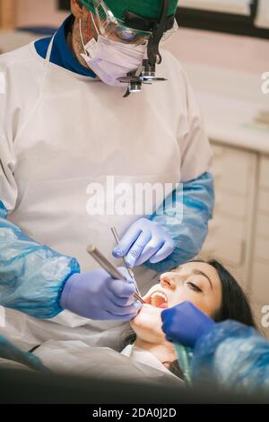 Anonymous orthodontist in uniform checking teeth of Woman using medical tools near crop nurse Stock Photo