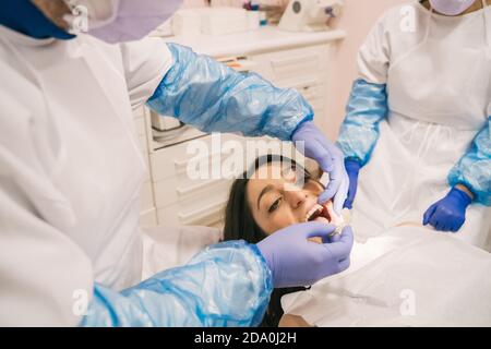 From above of crop unrecognizable orthodontist in sterile gloves putting transparent braces on teeth of Woman in clinic Stock Photo