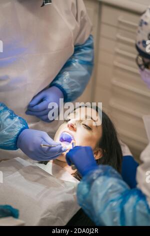 From above of anonymous orthodontist in uniform checking teeth of Woman using medical tools near crop nurse Stock Photo