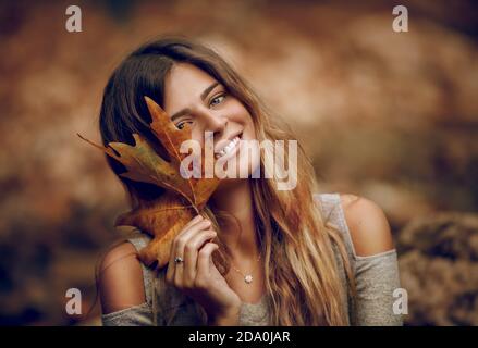 Portrait of a Beautiful Girl Having Fun in Autumn Forest. Holding in Hand Dry Maple Leaf. Beauty of Fall Season. Stock Photo