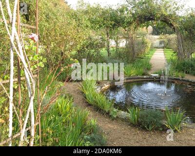 A view in the walled garden at Rousham House, Oxfordshire, with its smalll pond & fountain, herbaceous borders and formal pathways. Stock Photo