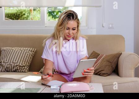 Focused female freelancer sitting at table and taking notes while using tablet and working on startup project remotely from home Stock Photo