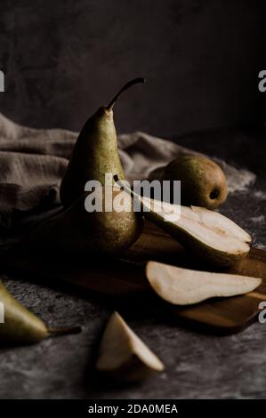 Whole and cut fresh ripe green pears arranged on table in dark studio Stock Photo