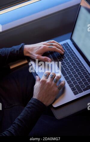 Crop young male freelancer sitting on passenger seat in modern train and typing on netbook while working during trip Stock Photo