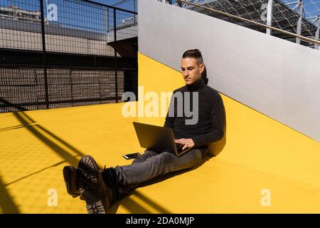 Concentrated man typing on netbook while having working day in park in sunny day Stock Photo