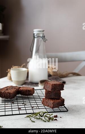 Pouring chocolate sauce from pot over stacked pieces of homemade brownie cake arranged on metal grid while preparing dessert in kitchen Stock Photo