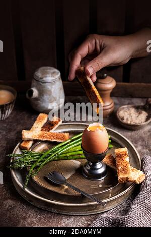 High angle of crop unrecognizable person dipping bread crouton in yolk of soft boiled egg served on table in kitchen for breakfast Stock Photo