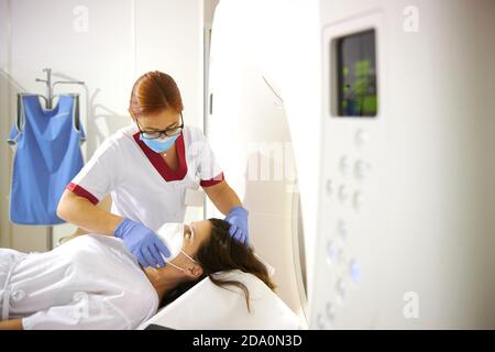 Doctor in uniform and eyeglasses using tomography machine with lying female patient in hospital Stock Photo