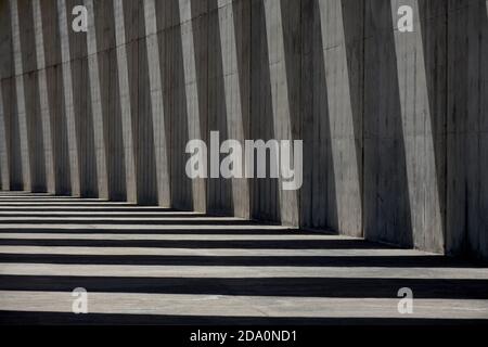 Columns of empty concrete walkway illuminated by sunlight casting lines of shadow on stone wall Stock Photo