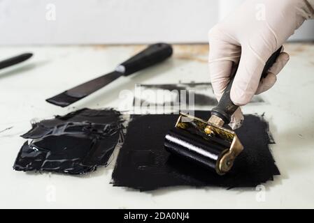 Closeup hand of crop anonymous artisan in glove using braver and spreading ink on sheet for engraving while working in professional workshop