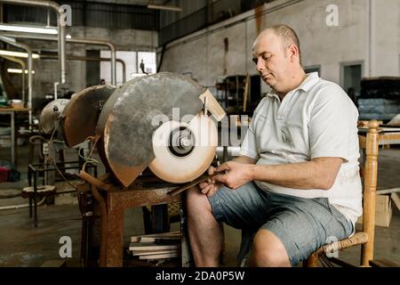 Craftsman using grinding machine while making creative wooden folding fan in shabby workshop Stock Photo