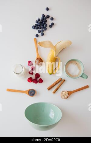 From above composition with fresh berries and banana with seeds and bottle of milk for healthy breakfast meal arranged with empty bowl on white table Stock Photo