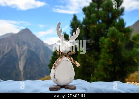 Green Christmas tree with cones growing in French Alps mountains, funny wooden toy christmas moose close up and peaks on background Stock Photo