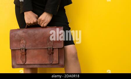 Crop anonymous female in skirt with stylish brown leather handbag standing against yellow background Stock Photo