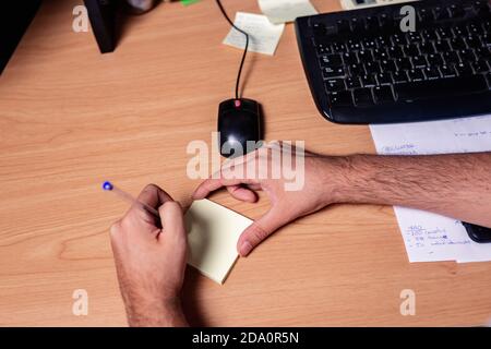 From above of crop anonymous office worker sitting at table in workplace and writing memo on sticky note during working day Stock Photo