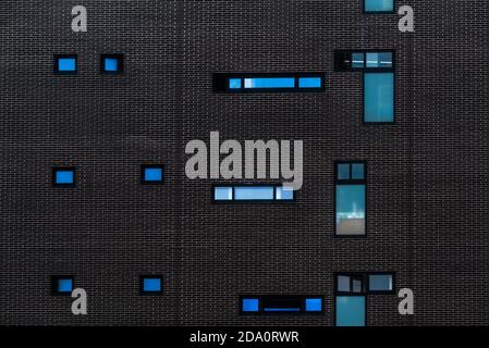 Abstract background of detail of modern building with dark wall with windows of different shapes and sizes Stock Photo