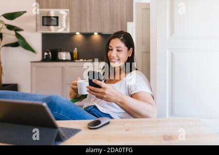 Smiley brunette girl using a smartphone in the modern kitchen Stock Photo
