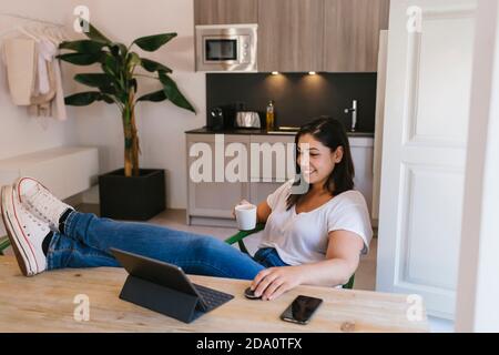 Relaxed and happy Woman working from kitchen at home Stock Photo