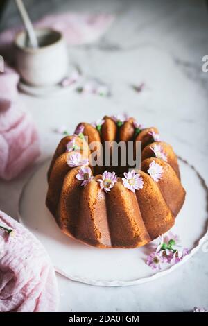 From above of tasty Bundt cake decorated with fresh flowers and served on plate on table in kitchen Stock Photo