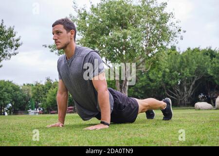 Low angle of strong male athlete doing push ups during training on green lawn in park Stock Photo