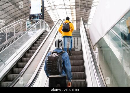 Back view of African American male friends wearing medical masks standing on escalator on modern train station Stock Photo