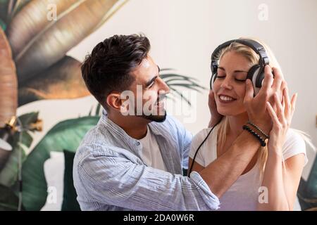 Side view of cheerful young man and Woman with headphones having fun and enjoying music while spending time together at home Stock Photo