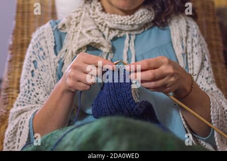 Front view of a woman sat on a rattan chair knitting. Stock Photo