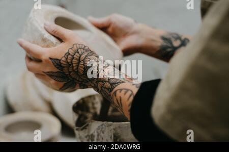 Side view of crop anonymous tattooed artisan pouring clay in bowl while creating pottery in studio Stock Photo
