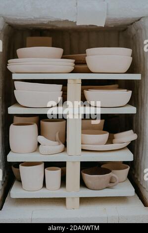 Collection of various ceramic pots and earthenware placed on wooden shelves in art studio Stock Photo