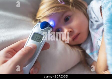 Parent takes temperature for her child with infrared thermometer at home, low-grade fever Stock Photo